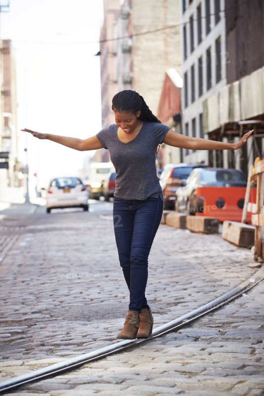 Black woman balancing on track in cobblestone city street