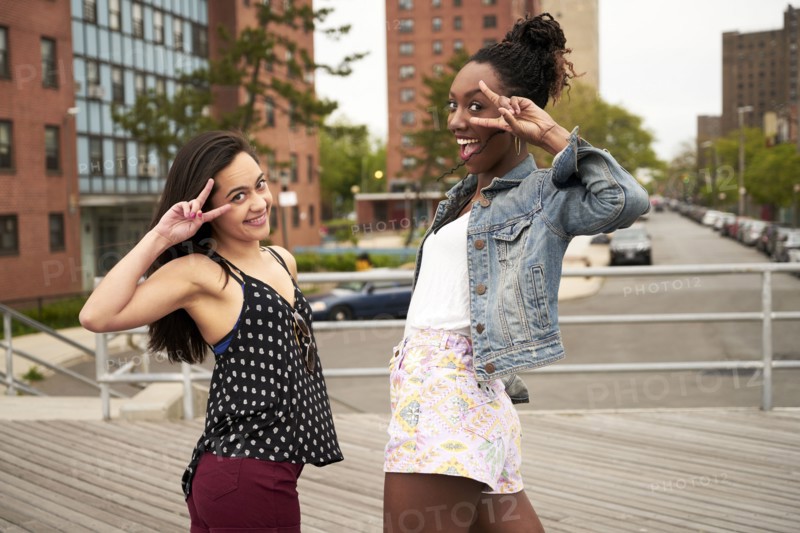 Smiling women gesturing peace on city boardwalk
