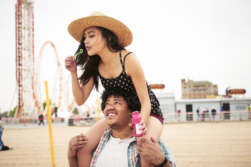 Man carrying woman blowing bubbles on shoulders at beach