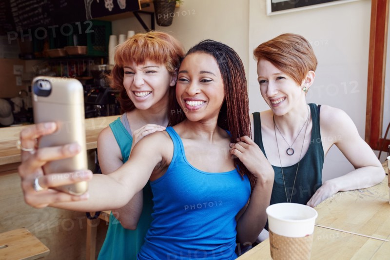 Smiling women posing for cell phone selfie in coffee shop