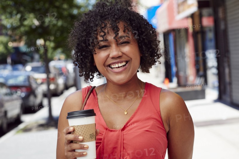 Smiling woman carrying coffee on city sidewalk