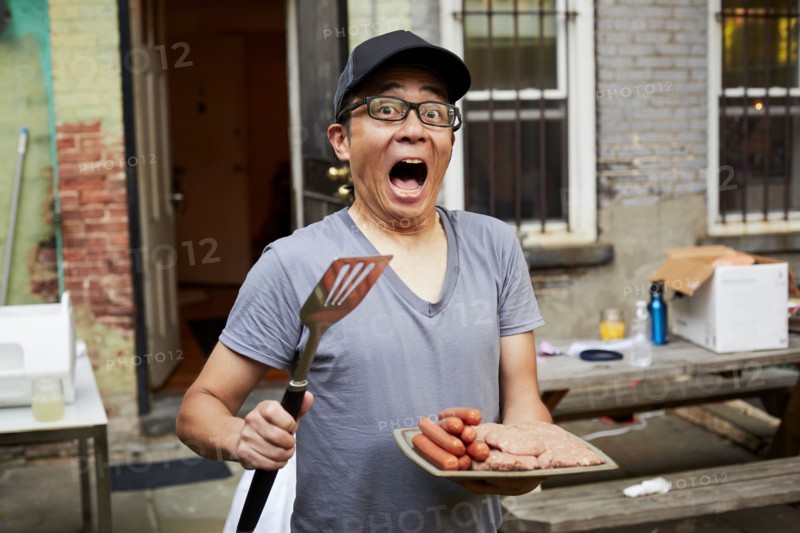 Surprised Japanese man holding plate of raw meat in backyard