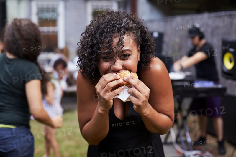 Mixed Race woman eating hamburger at backyard party