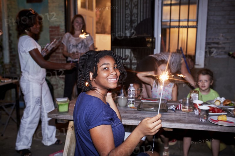 Smiling girl holding burning sparkler at backyard party