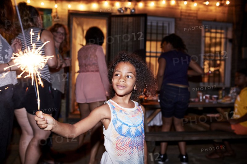 Smiling girl holding burning sparkler at backyard party