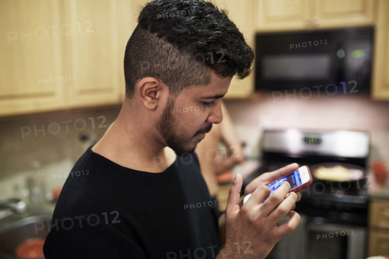 Middle Eastern man texting on cell phone in kitchen