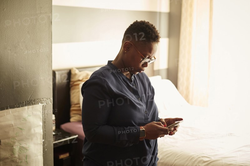 Black woman standing in bedroom texting on cell phone