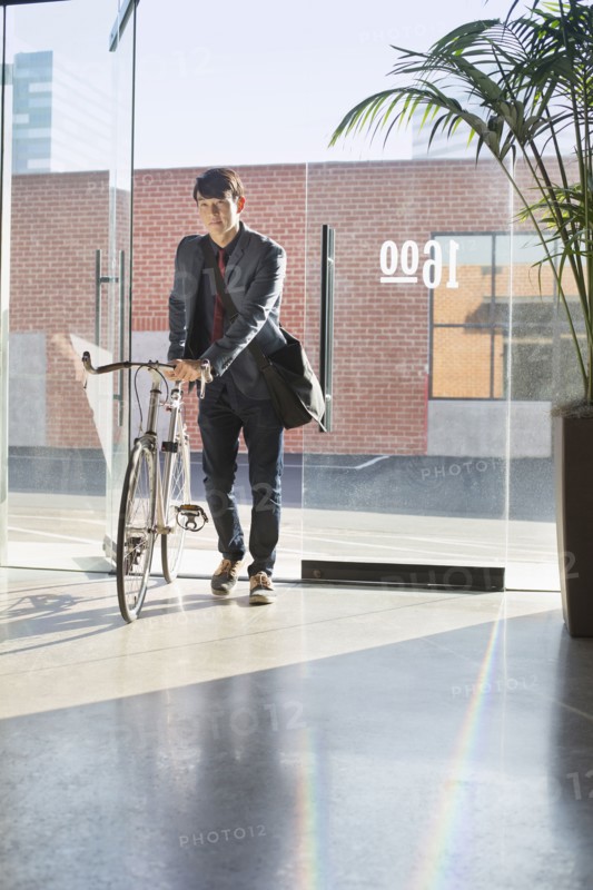 Korean businessman wheeling bicycle in office
