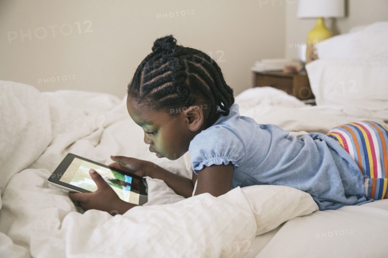 African American girl using digital tablet on bed