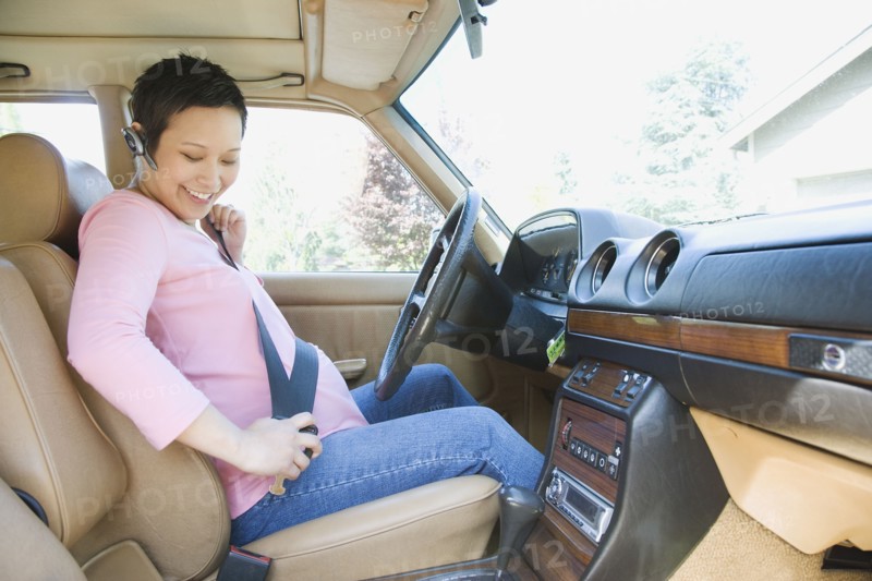 Pregnant woman putting on seatbelt in car