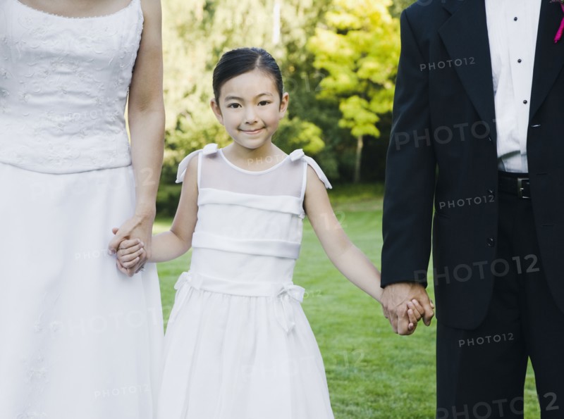 Asian newlyweds holding flower girl's hands