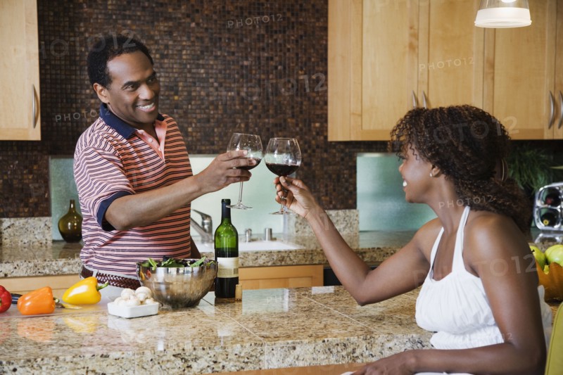 African couple toasting with red wine in kitchen