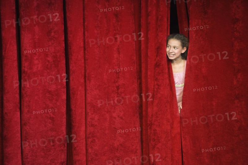 Mixed race person hiding behind stage curtain
