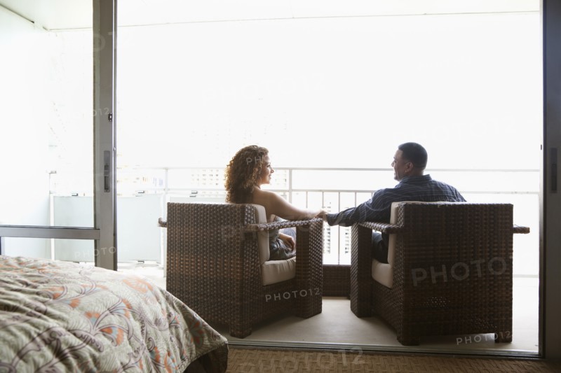 Couple sitting in armchairs and holding hands on urban balcony