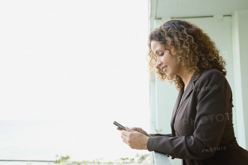 Hispanic woman text messaging on balcony