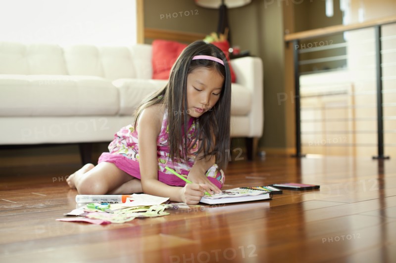 Mixed race girl writing in book on floor