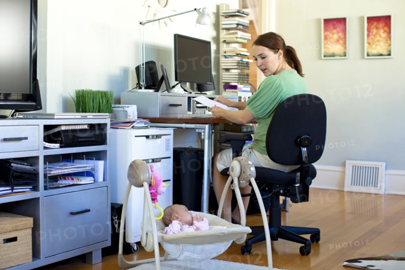 Caucasian mother working in home office with baby next to her