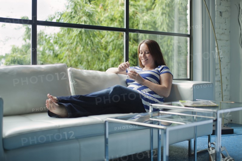Pregnant Caucasian woman eating on sofa
