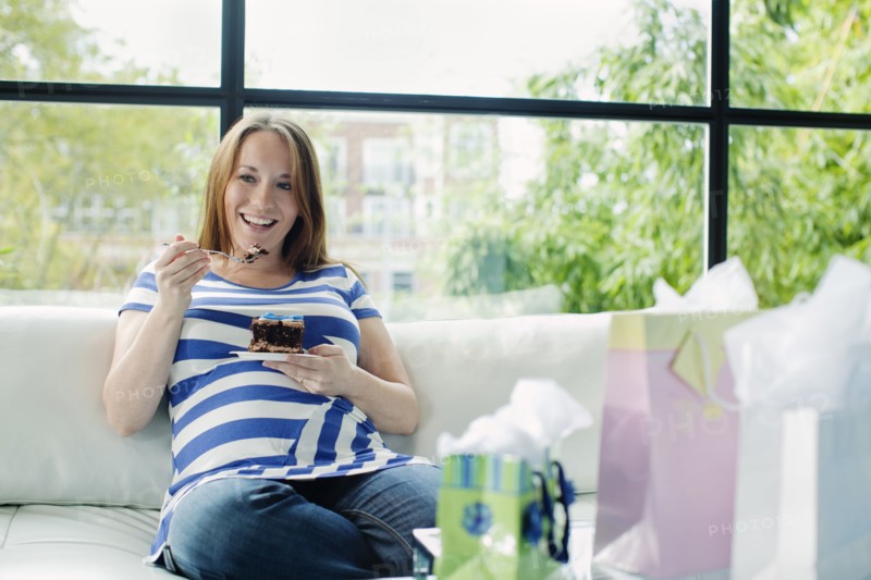 Pregnant Caucasian woman eating on sofa at baby shower