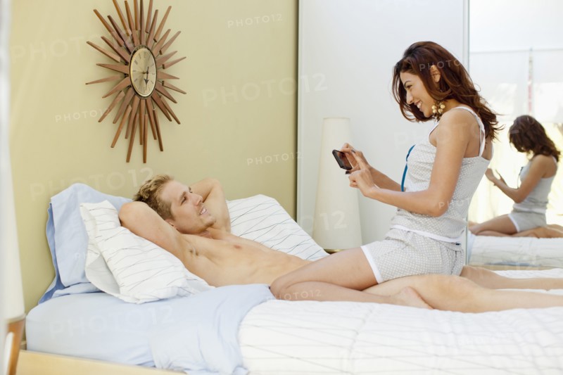 Woman taking picture of boyfriend in bed