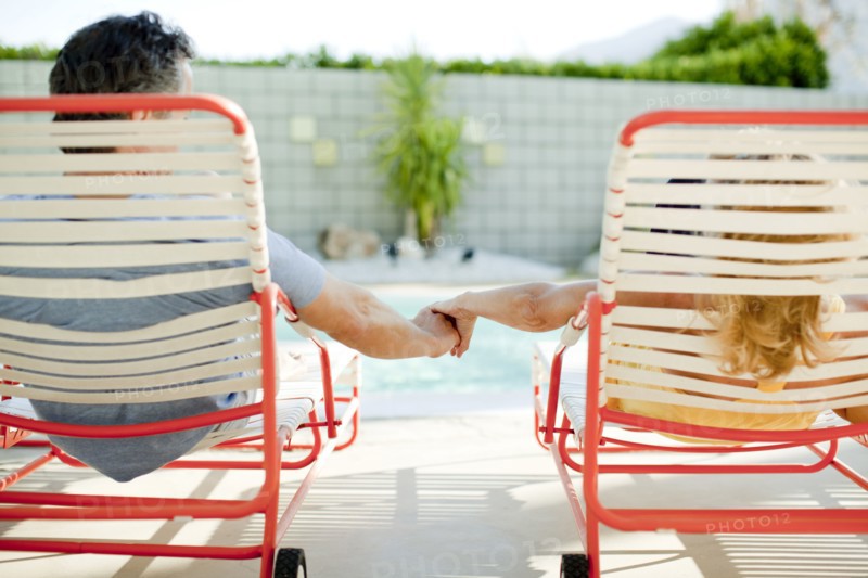 Couple holding hands in lounge chair near swimming pool