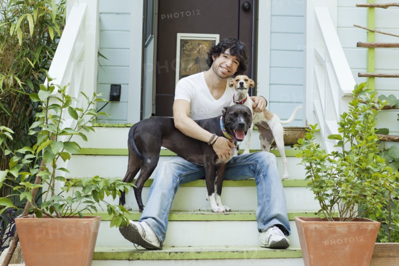 Mixed race man sitting on front stoop with dogs