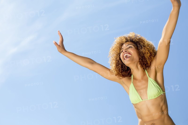 Mixed race woman in bikini with arms raised