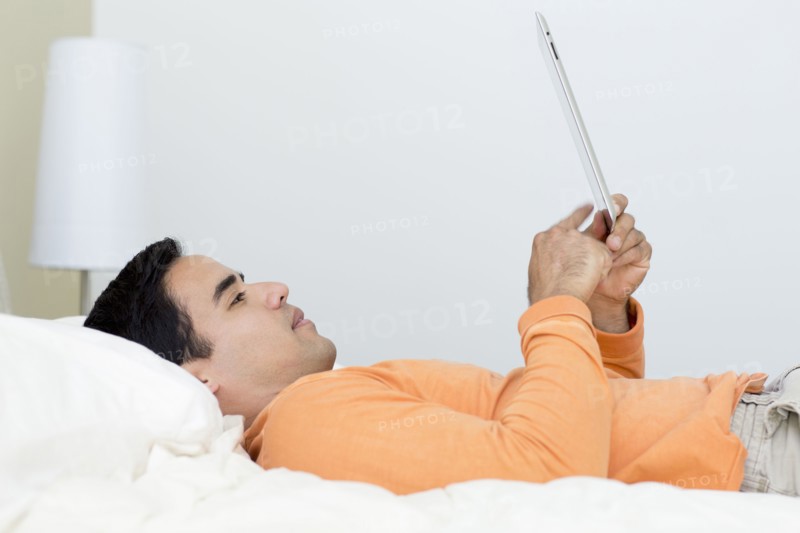 Mixed race man laying in bed using digital tablet