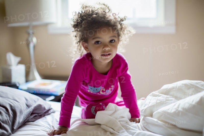 Mixed race girl kneeling on bed