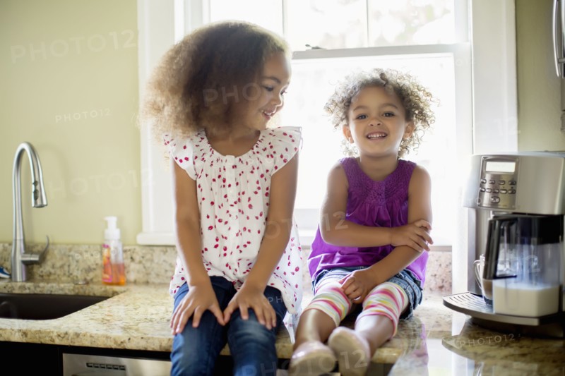 Mixed race sisters sitting on kitchen counter