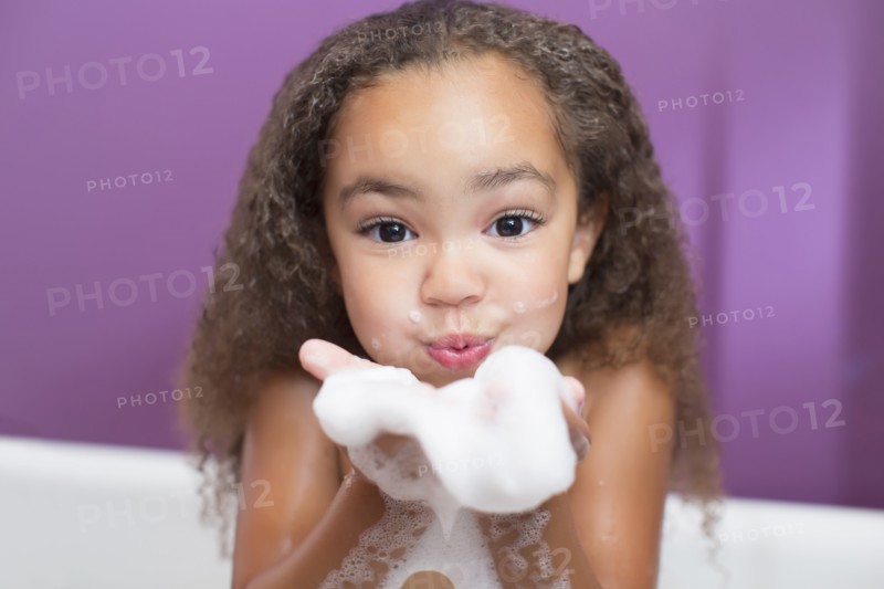 Mixed race girl playing with bubbles in bathtub