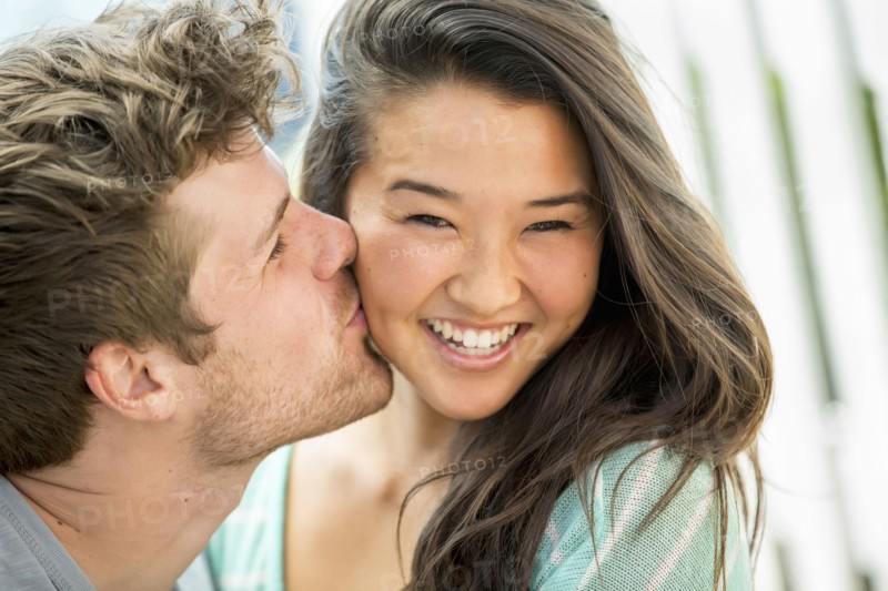 Man kissing girlfriend's cheek outdoors