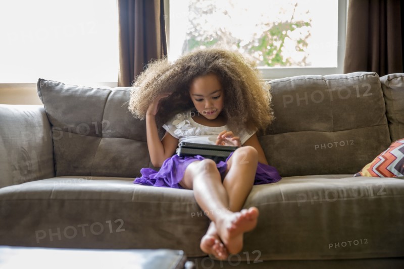 Mixed race girl using digital tablet on sofa