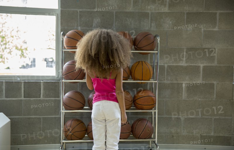 Mixed race girl picking basketball from rack