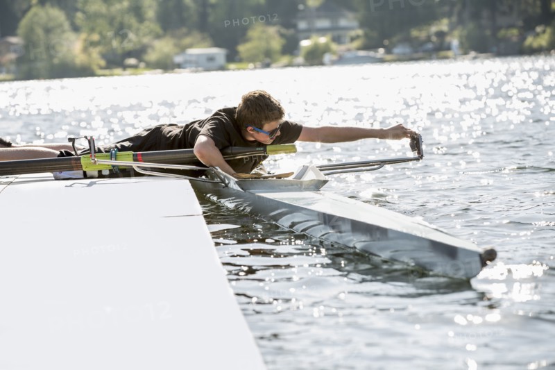 Teenage boy preparing scull from dock over lake