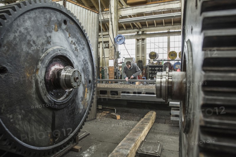 Caucasian man working behind metal cogs in metal shop