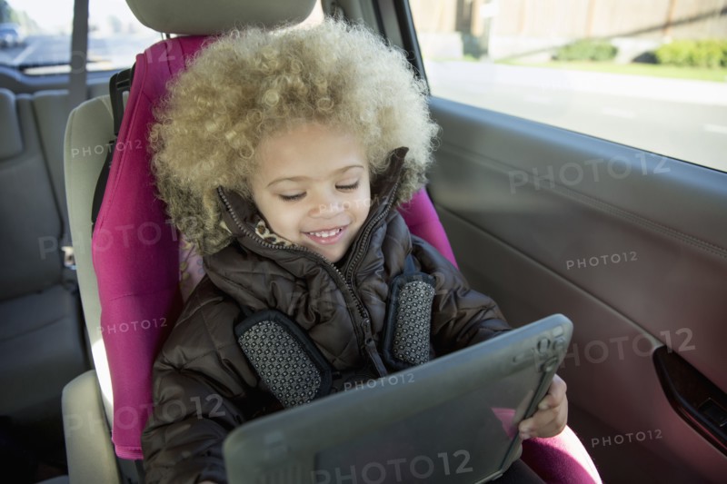 Mixed race girl using digital tablet in back seat of car