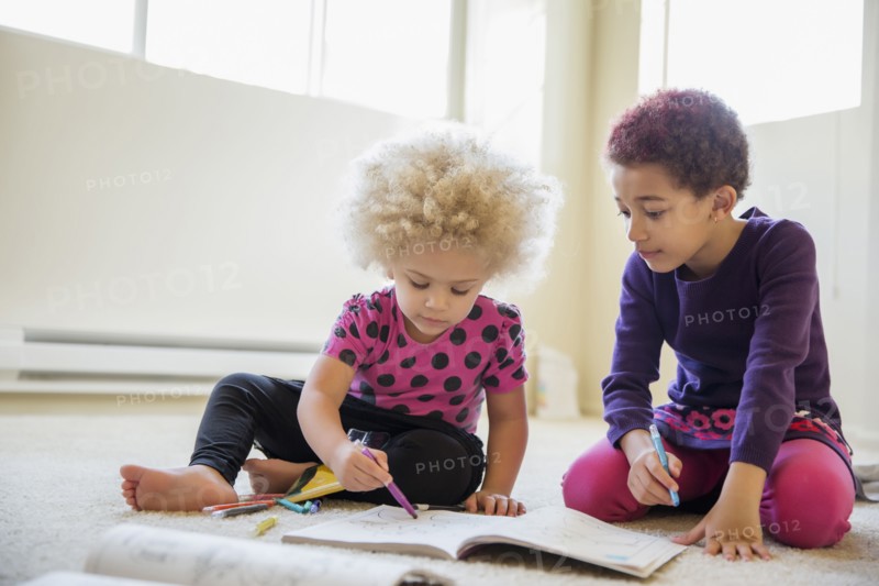 Mixed race sisters coloring on floor