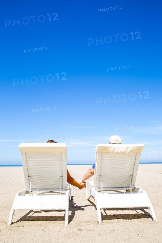 Couple holding hands in lounge chairs on beach