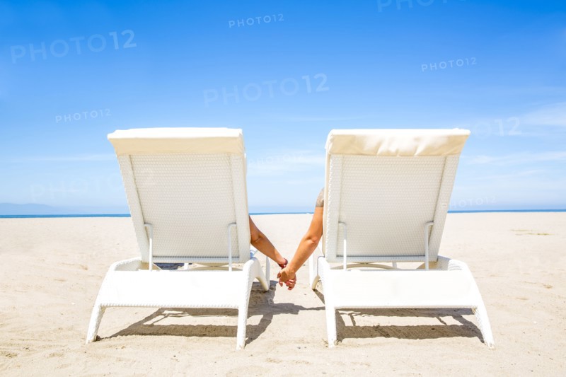 Couple holding hands in lounge chairs on beach