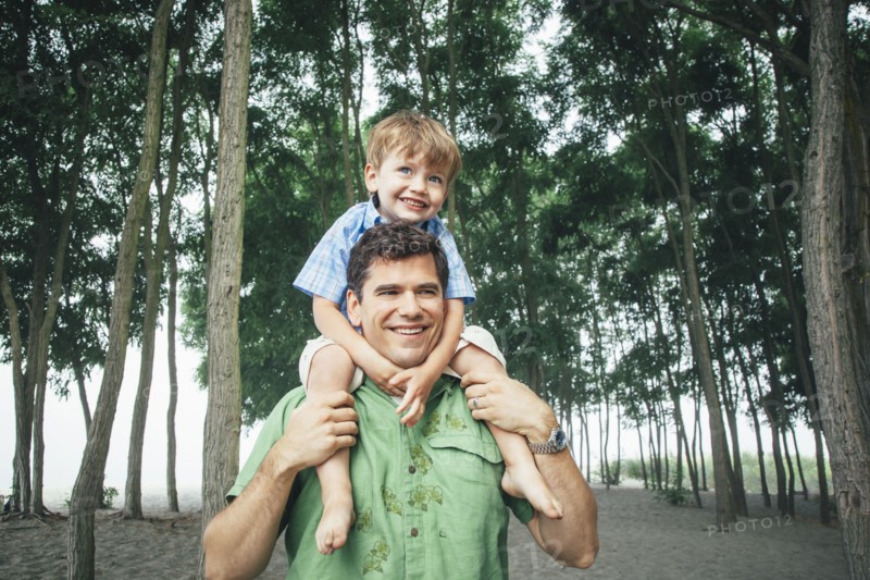Man carrying son on wooded beach