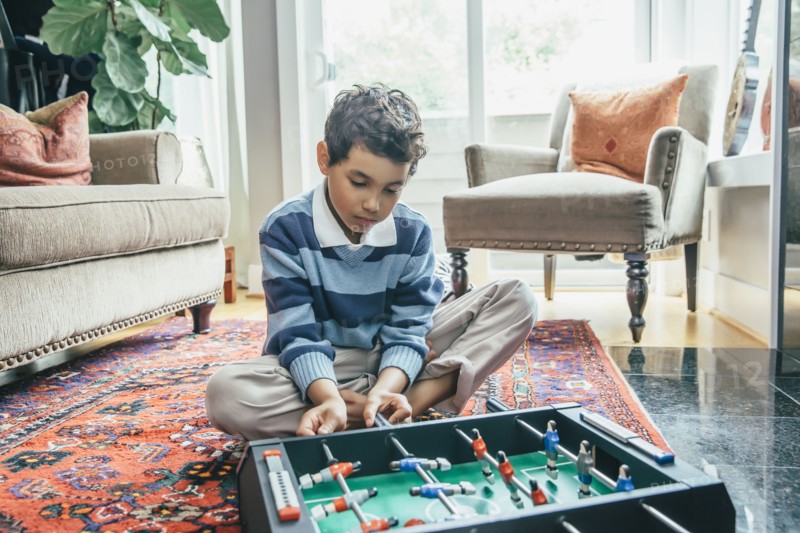 Mixed race boy playing foosball on living room floor