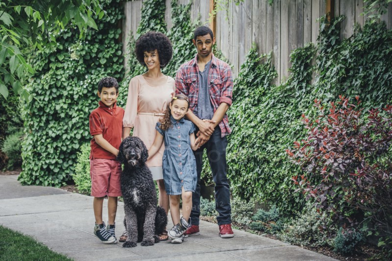 Mixed race mother and children smiling with dog on suburban sidewalk