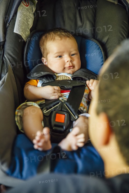 Caucasian father admiring baby boy in car seat