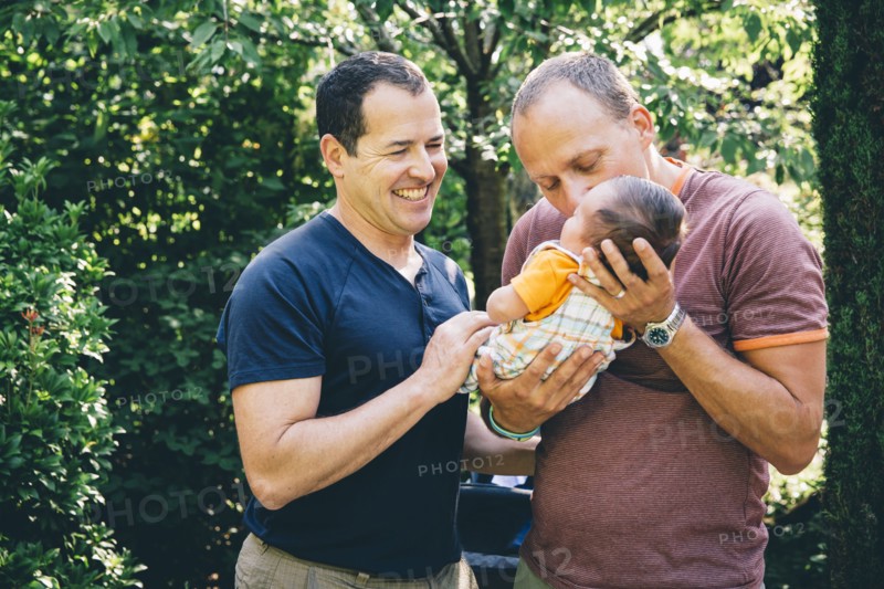 Caucasian gay couple kissing baby boy outdoors