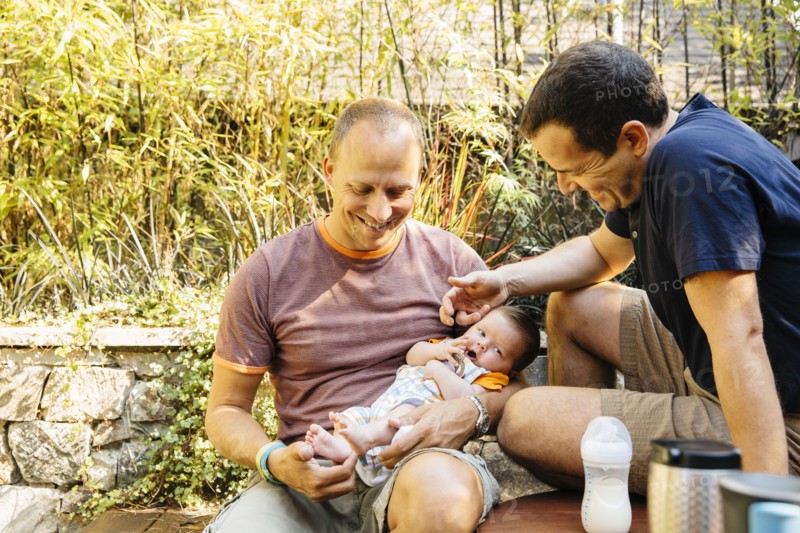 Caucasian gay couple admiring baby boy in backyard