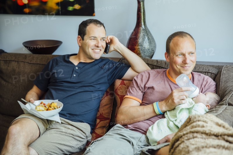Caucasian gay couple relaxing with baby boy on sofa
