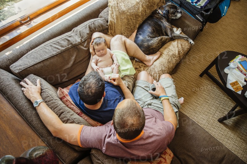 Caucasian gay couple holding sleeping baby boy on sofa