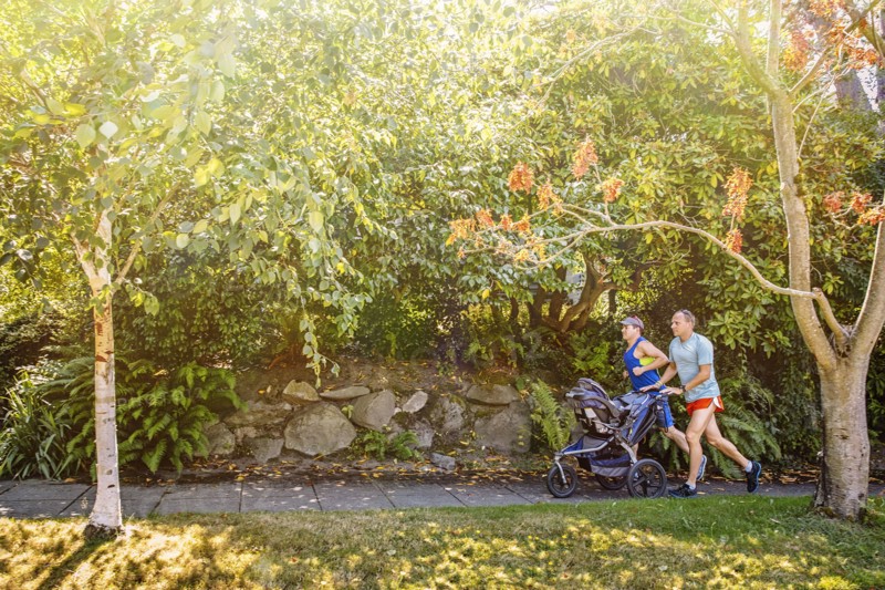 Caucasian gay couple jogging with stroller on sidewalk