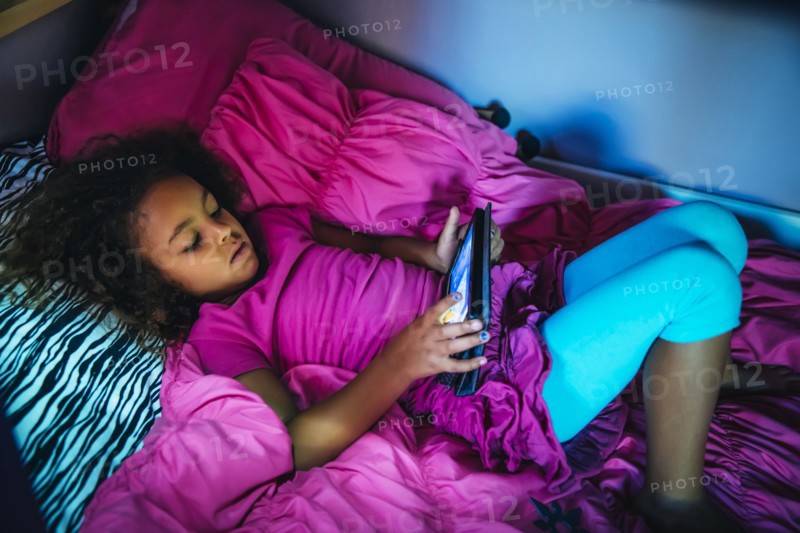 Mixed race girl using digital tablet on bed